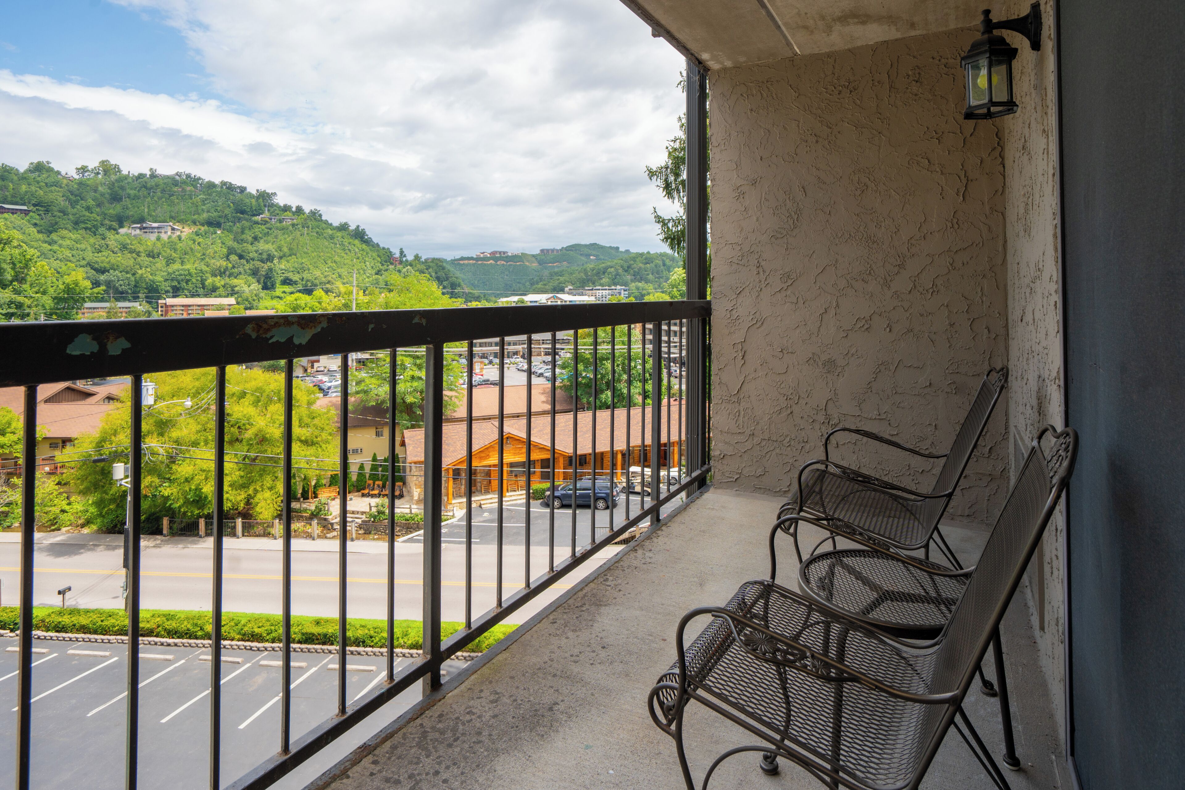 A balcony with a view of a parking lot and buildings, a metal railing, and a single bench.