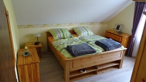A single bed with a wooden frame, green and white striped bedding, and two pillows. There is a nightstand with a lamp and a small table with a flower vase. - Apartment house Monika (Bergenhausen)