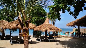 A beach with palm trees, thatched umbrellas, and beach chairs.