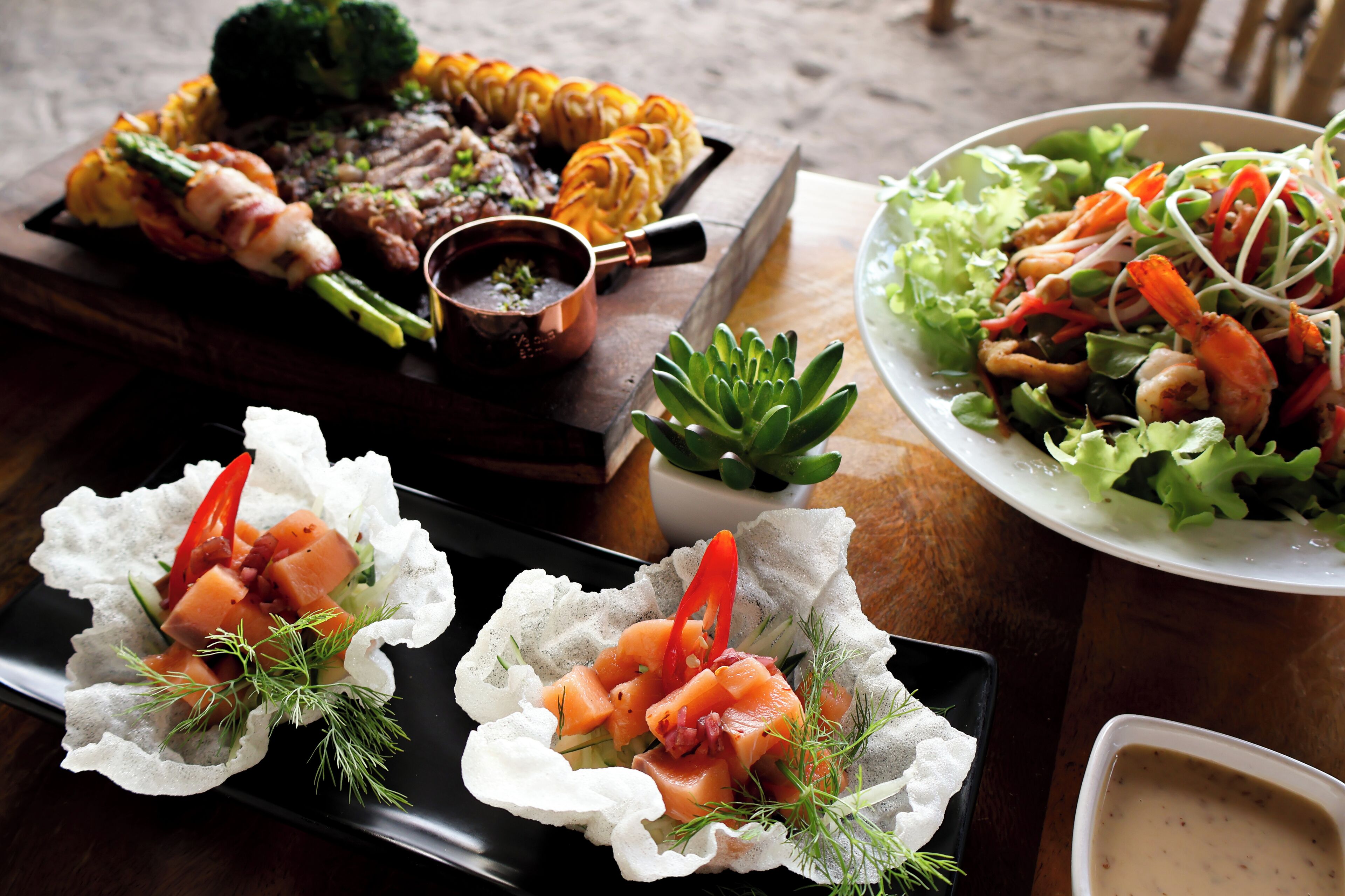 Variedad de platillos, incluyendo carnes a la parrilla, mariscos y ensaladas, sobre una mesa de madera.