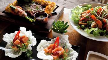 Variedad de platillos, incluyendo carnes a la parrilla, mariscos y ensaladas, sobre una mesa de madera.
