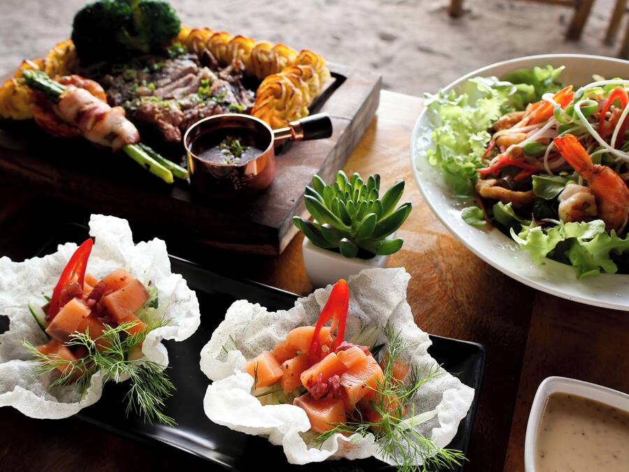 Variedad de platillos, incluyendo carnes a la parrilla, mariscos y ensaladas, sobre una mesa de madera.