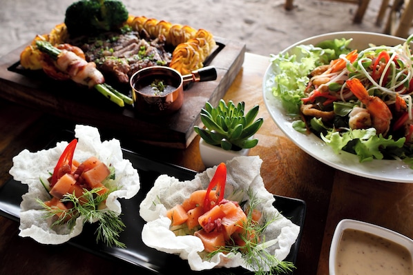 A variety of dishes including grilled meats, seafood, and salads, presented on a wooden table. - The Lazy Lodge (Ko Lanta)