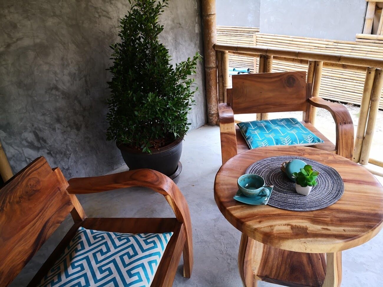 Een houten tafel met een geweven placemat, twee stoelen met gestreepte kussens en een pot met een plant.