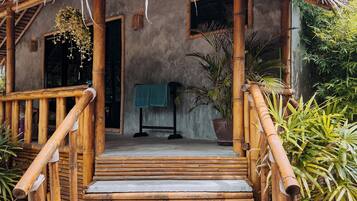 A rustic building with a thatched roof, a wooden staircase leading to a porch, and a concrete floor.