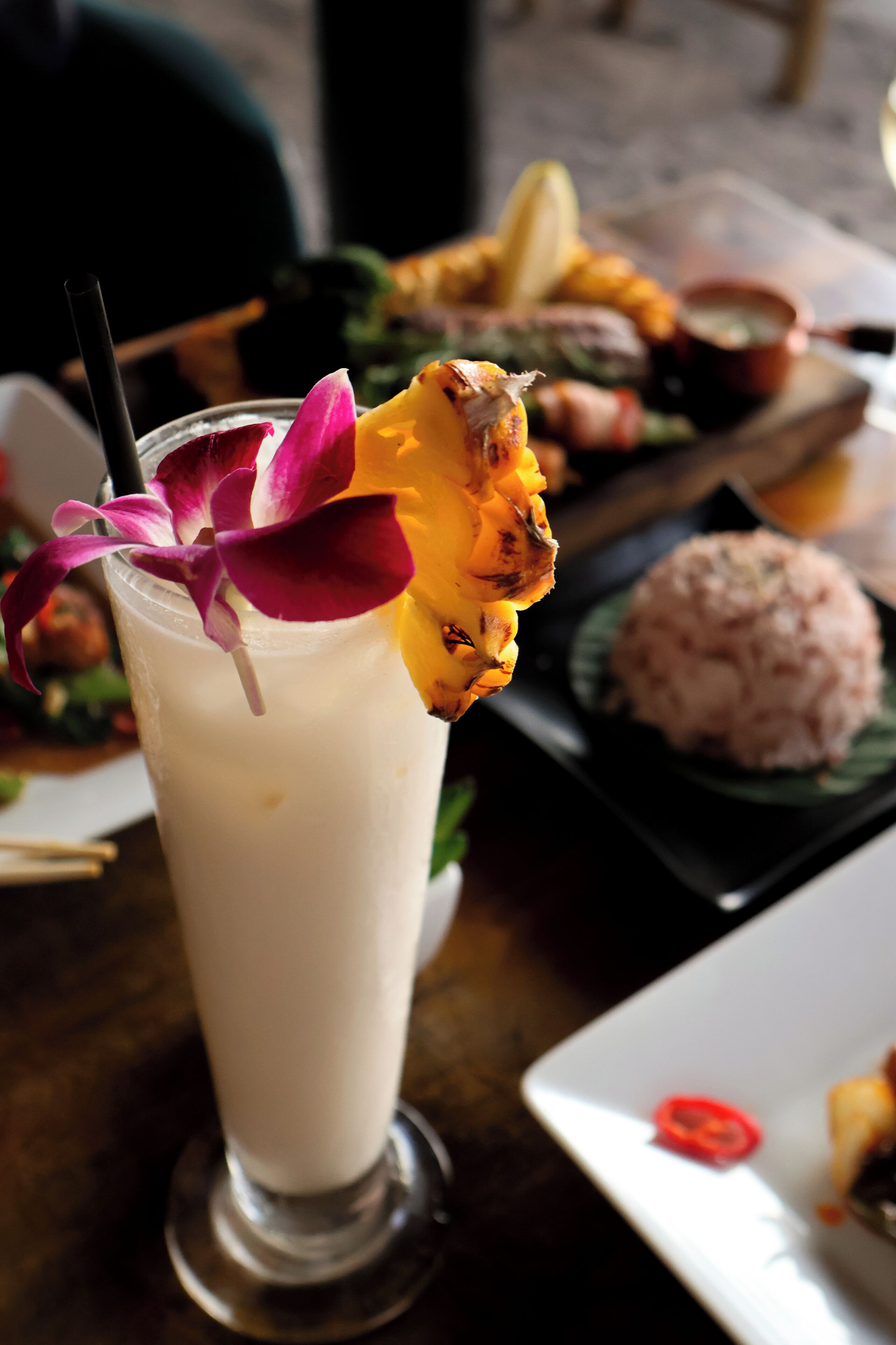 A dessert drink with a flower garnish, a plate of food, and a small bowl of sauce.