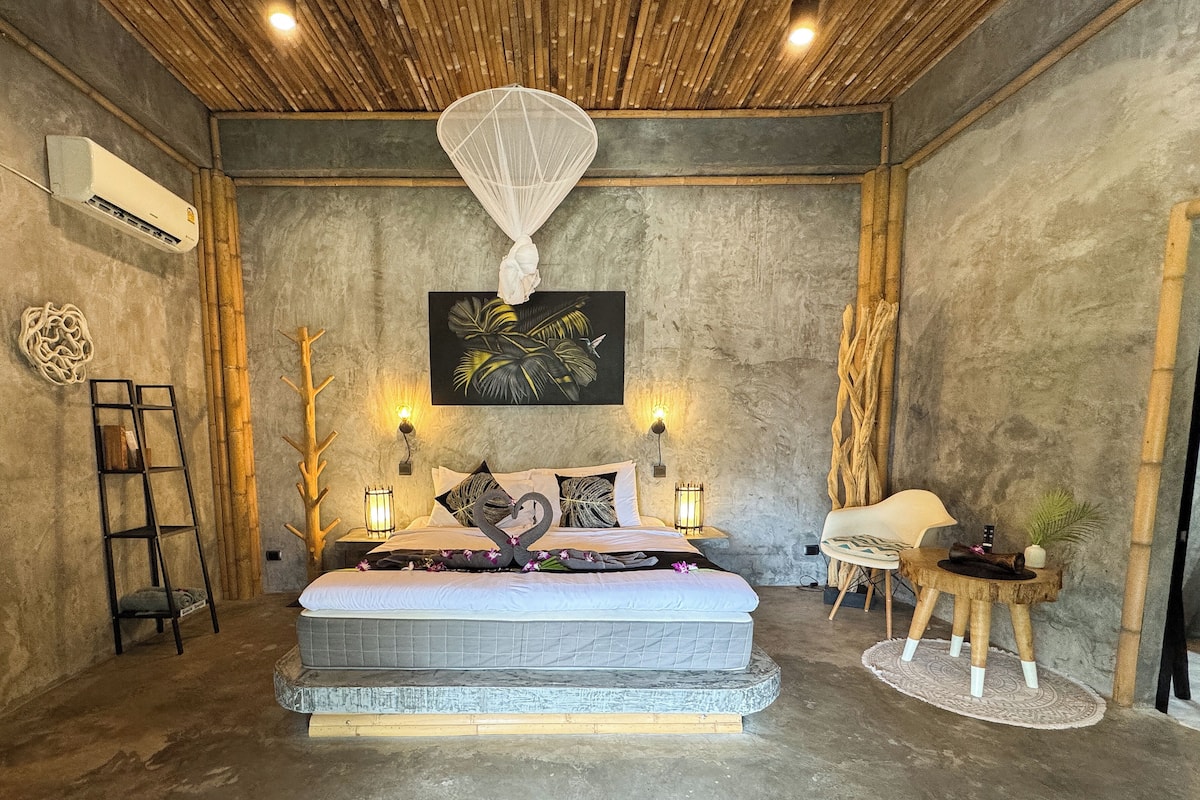 A bedroom with a large bed, a wooden ceiling, a wall-mounted air conditioner, and a tropical-themed painting.
