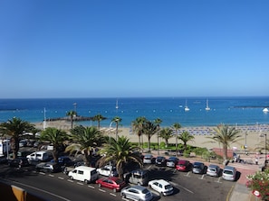 Un parking rempli de voitures, avec une plage en arrière-plan.