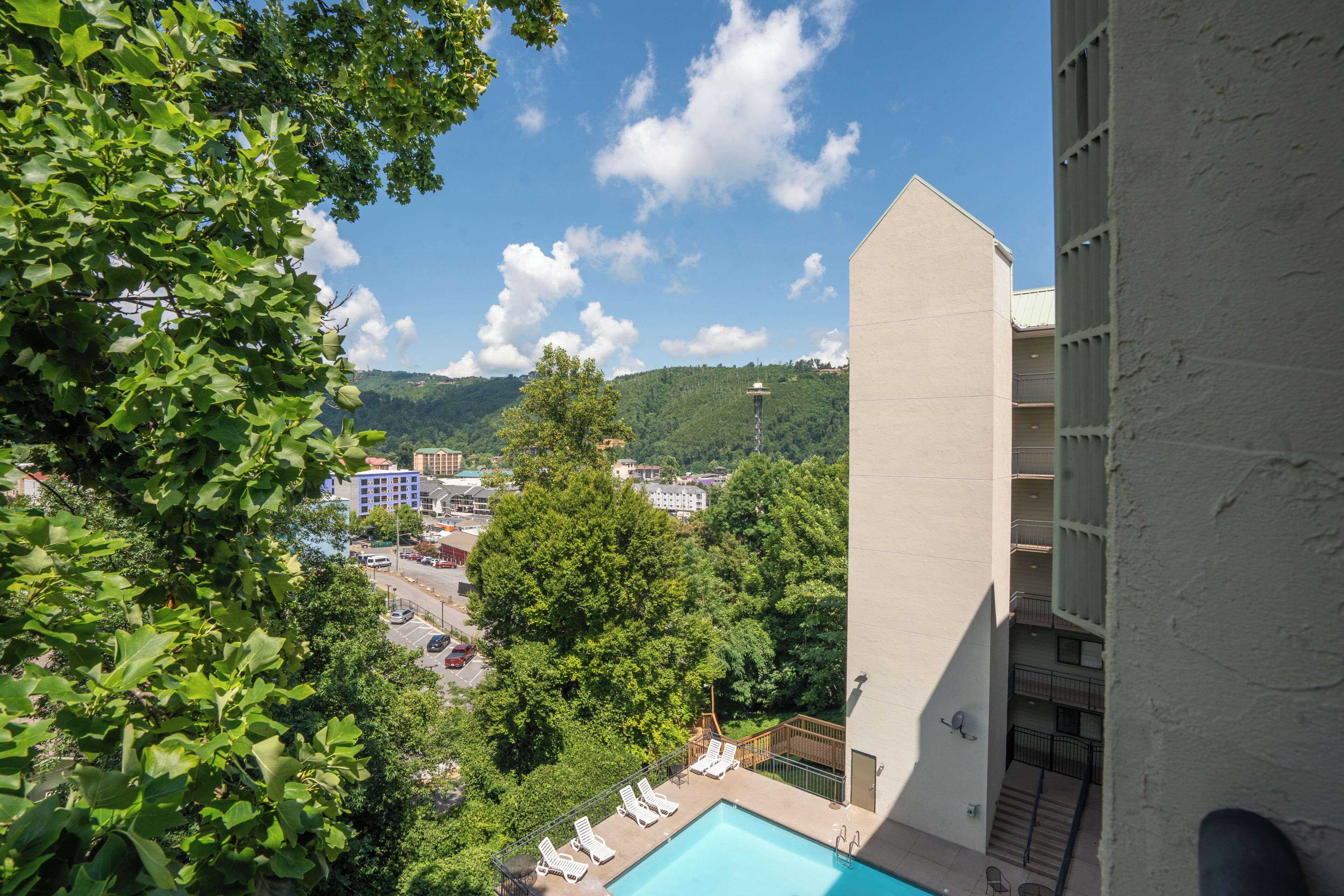 Une vue d’un hôtel avec une piscine, entouré de verdure et avec des bâtiments en arrière-plan.