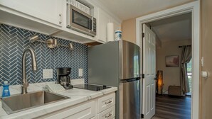 Una cocina con un refrigerador de acero inoxidable, un microondas y un lavamanos. Hay armarios y un salpicadero con motivo de espiga.