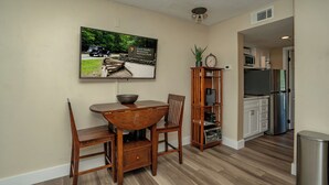 Un comedor con una mesa y sillas de madera, un televisor montado en la pared y una cocina al fondo.