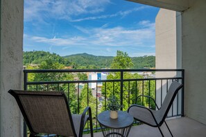 A balcony with two chairs and a small table, overlooking a green landscape and buildings. - Laurel Inn 508 is a beautiful condo with private balcony close to downtown (Gatlinburg)