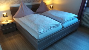 A double bed with two pillows, a nightstand with a lamp, and a patterned wallpaper. - Holiday home Nice view for 1 - 5 persons (Esch)