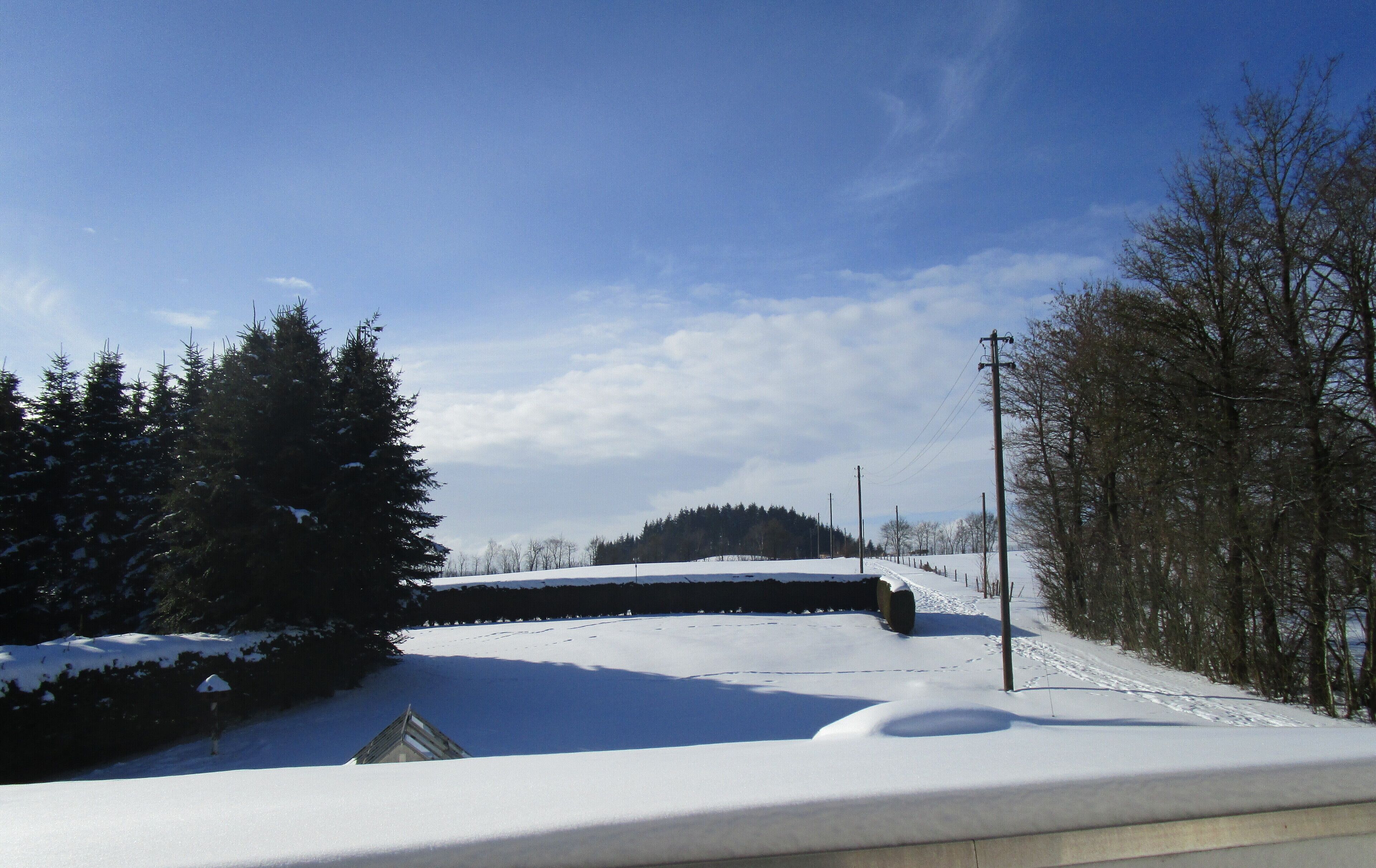 A snowy landscape with a clear sky, a road, and a building with a sloped roof.