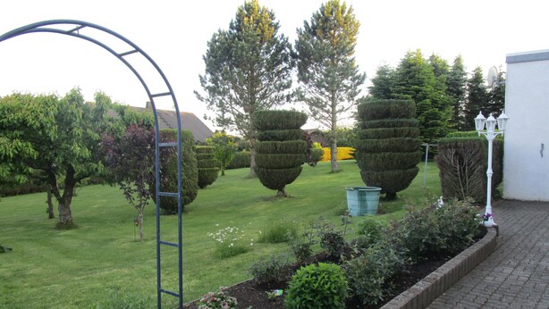 A garden with neatly trimmed hedges, a metal archway, and a variety of trees. - Holiday home Nice view for 1 - 5 persons (Esch)