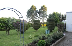 Um jardim com sebes bem aparadas, um arco de metal e diversas árvores.