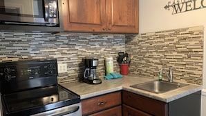 A kitchen with a stainless steel stove, a microwave, wooden cabinets, a tiled backsplash, a coffee maker, and a sink.