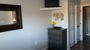 A bedroom with a bed, dresser, TV, and a mirror.