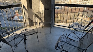 A balcony with metal chairs and tables, overlooking a parking area and buildings.