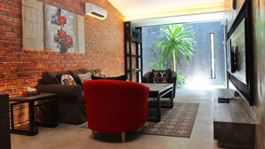 A modern living room with a brick wall, a red armchair, a sofa, a coffee table, and a flat-screen TV. - Owl Homestay (Kuala Lumpur)