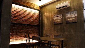 A dining area with a brick wall, wooden table, chairs, and artwork on the wall. - Owl Homestay (Kuala Lumpur)