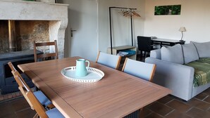 Un comedor con una mesa de madera, sillas, una jarra azul y una chimenea.