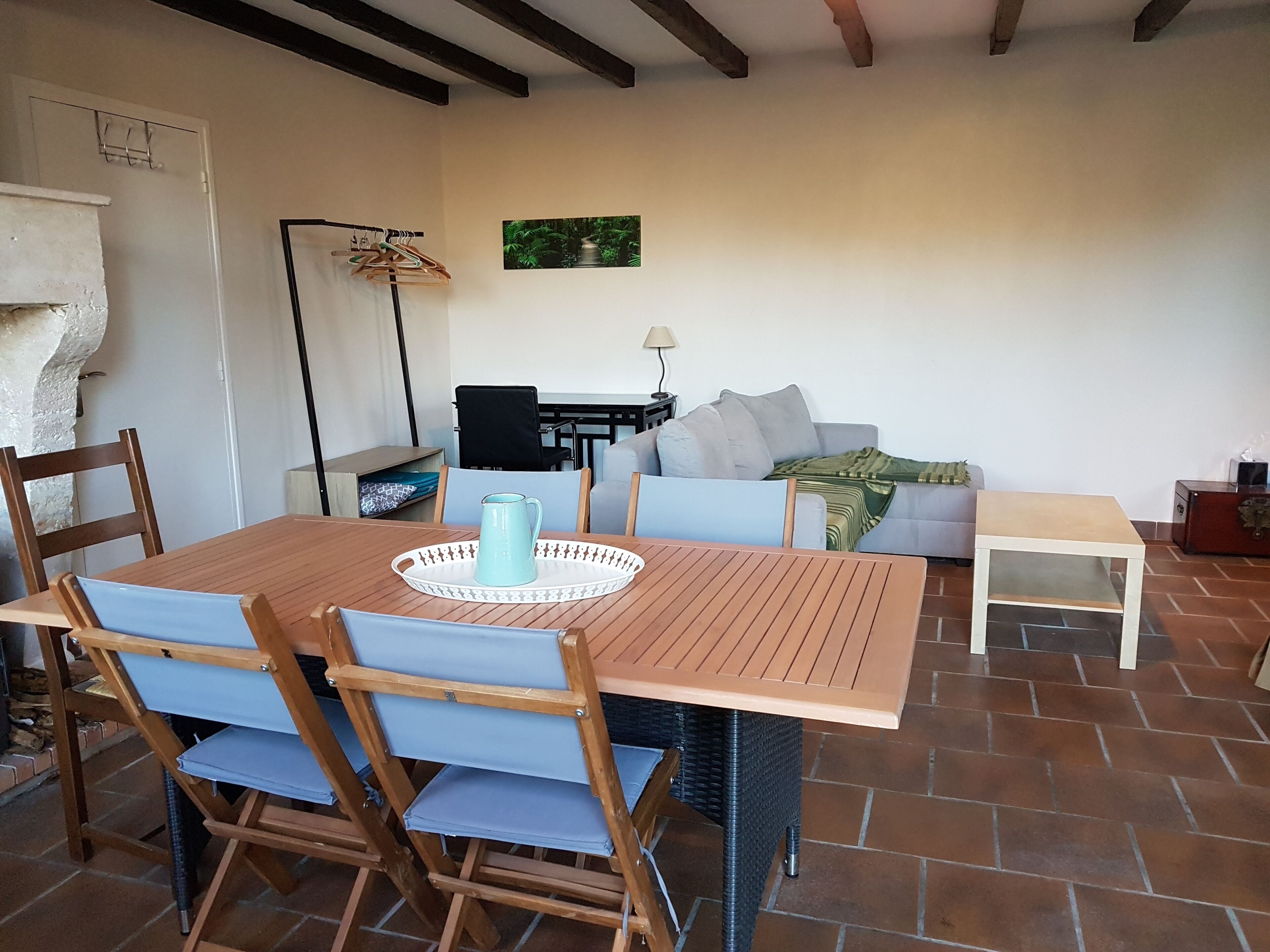 Un coin repas comprenant une table et des chaises en bois, une petite table d’appoint, un canapé et une lampe.