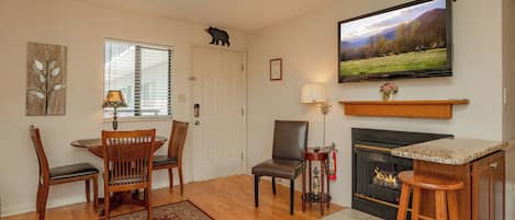 A living room with a fireplace, a television mounted above it, and a dining area with chairs and a table.