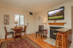 Una sala de estar con chimenea, un televisor montado encima y un comedor con sillas y una mesa.
