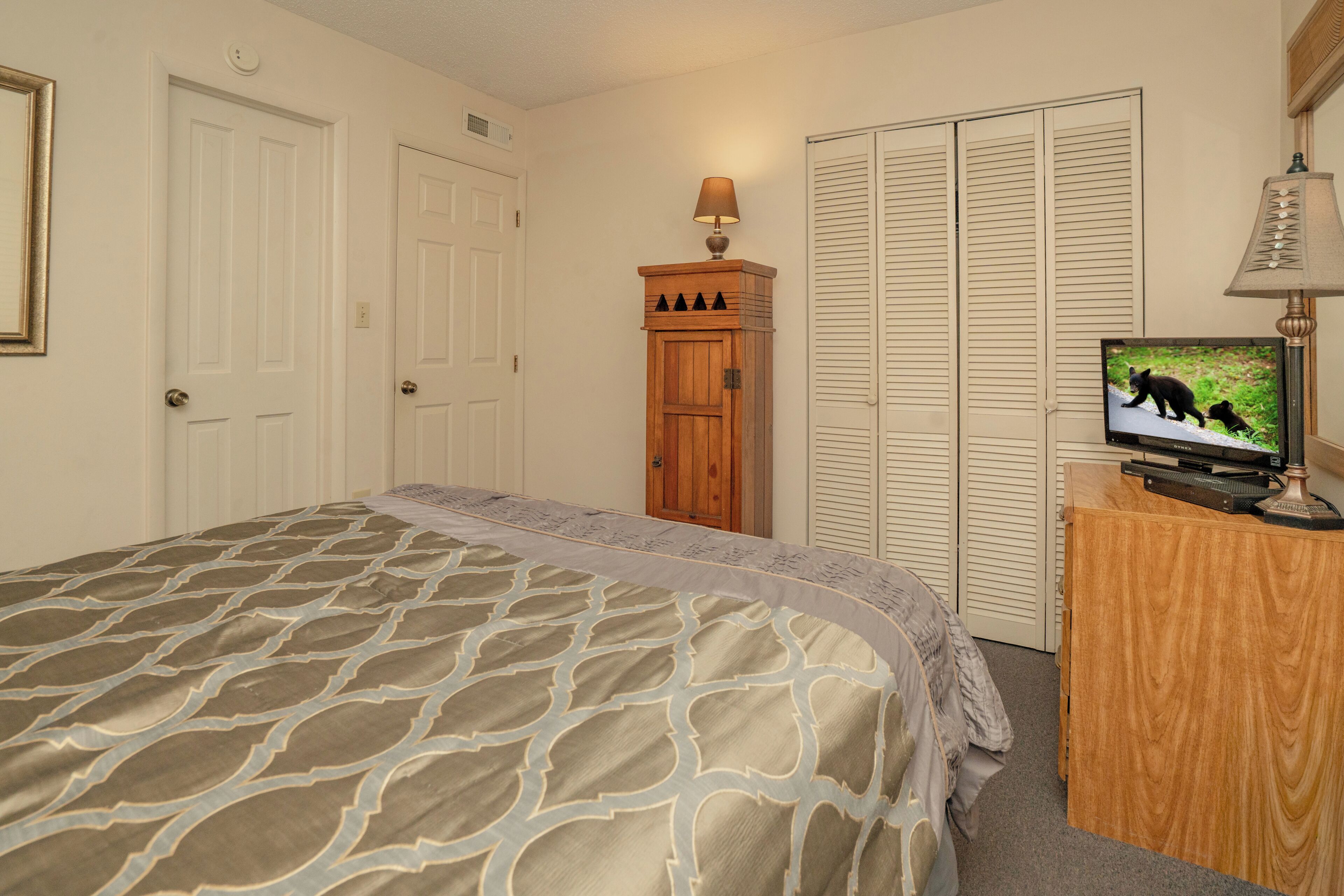 Une chambre à coucher comprenant un lit, une armoire en bois, un téléviseur et un placard aux portes à persiennes.