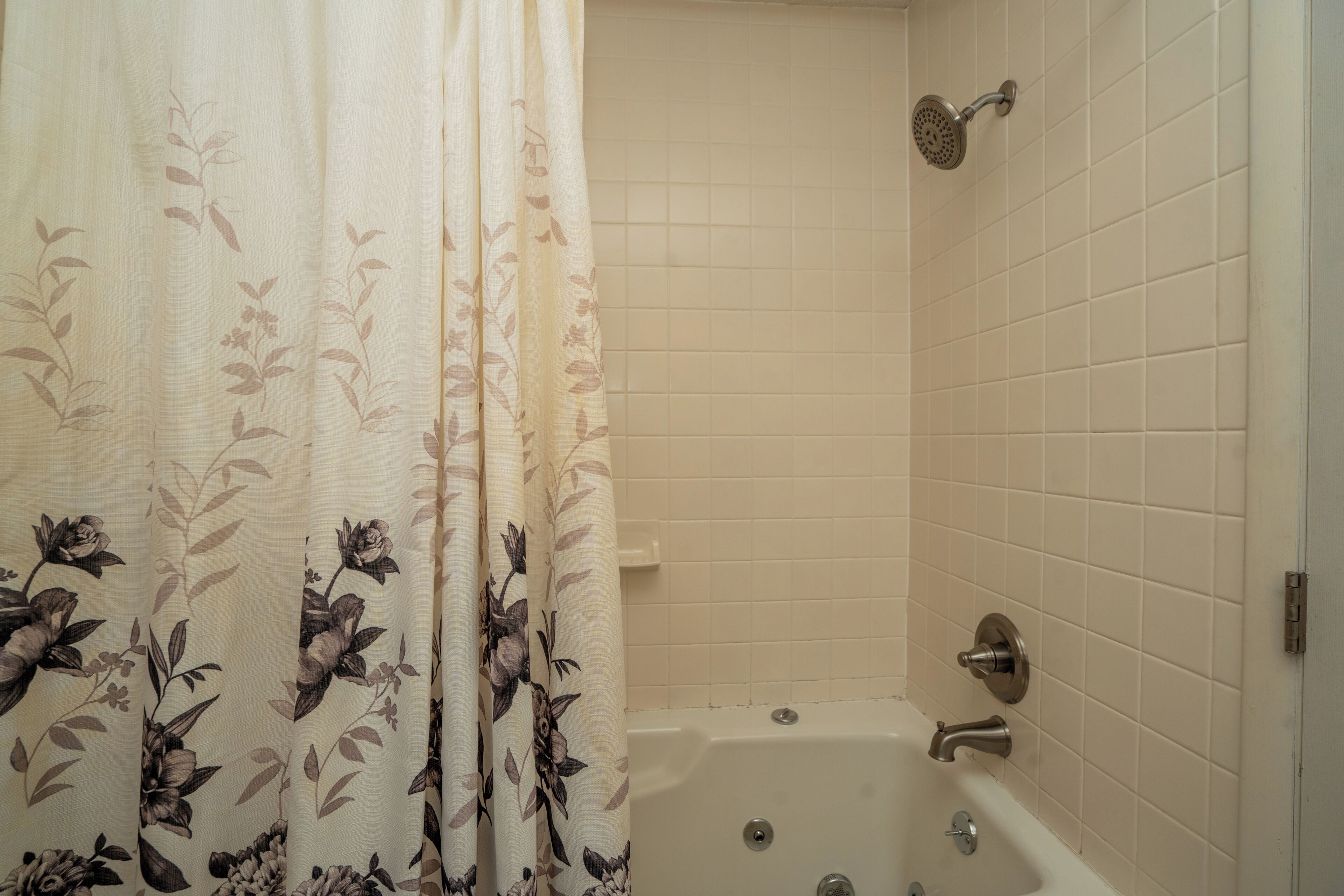 A bathroom with a bathtub, a showerhead, and a curtain with a floral pattern.