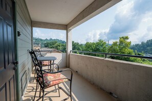 Un balcón con mesa y sillas, con vistas a una colina con árboles y casas.