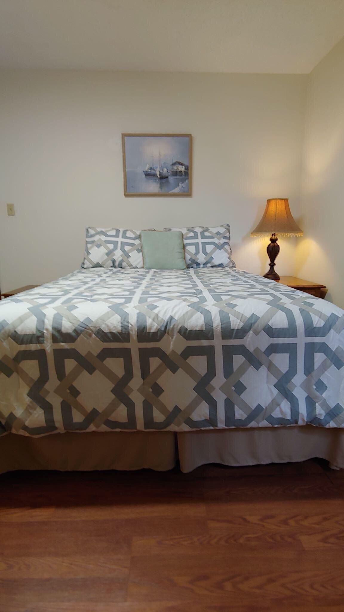 A bedroom with a bed, a nightstand, a lamp, and a painting on the wall.