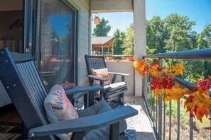 A balcony with two chairs and a table, a glass door, and a view of a house and trees.