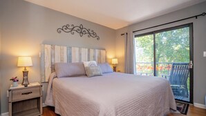 Une chambre dotée d’un grand lit, de deux tables de chevet avec des lampes, d’un élément décoratif mural et offrant une vue sur l’extérieur grâce à une porte-fenêtre coulissante.