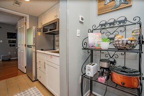 A kitchen with white cabinets, a stainless steel refrigerator, a black metal shelf with kitchen appliances, and a wall-mounted thermostat.