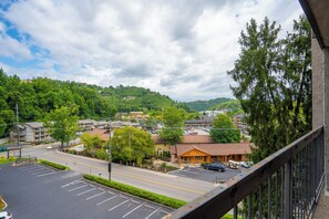 Blick auf einen Parkplatz mit einem Gebäude im Vordergrund, umgeben von Bäumen und einer hügeligen Landschaft im Hintergrund.