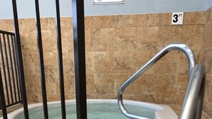 Ein Poolbereich mit Whirlpool, Metallhandlauf und mit Fliesen belegten Stufen zum Pool.