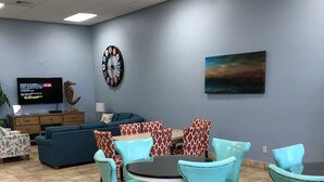 Ein moderner Loungebereich mit einem runden Tisch und passenden Stühlen, einem Flachbildfernseher, einer Uhr und einem Bild an der Wand.