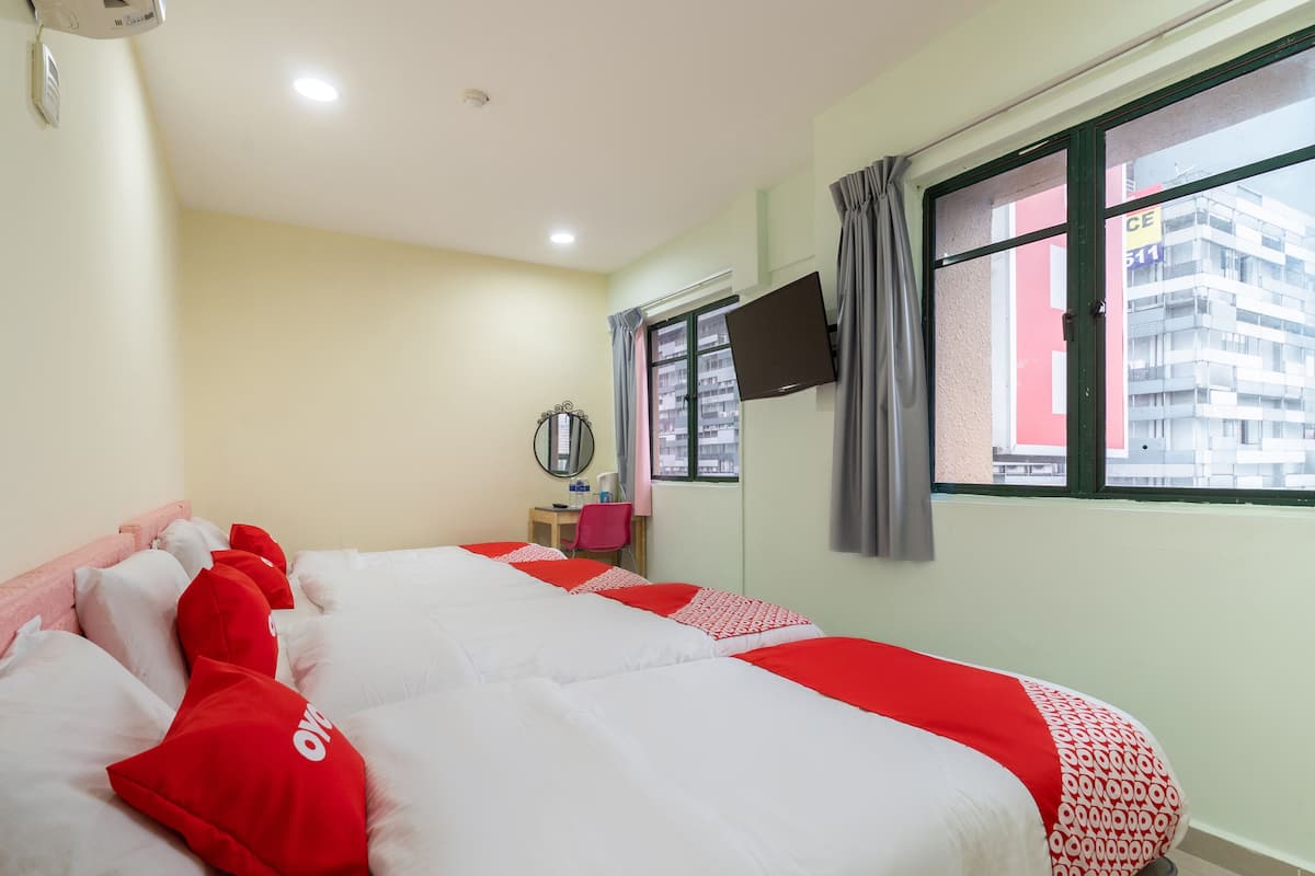 A hotel room with two beds, a desk, a chair, a TV, and a window with curtains.