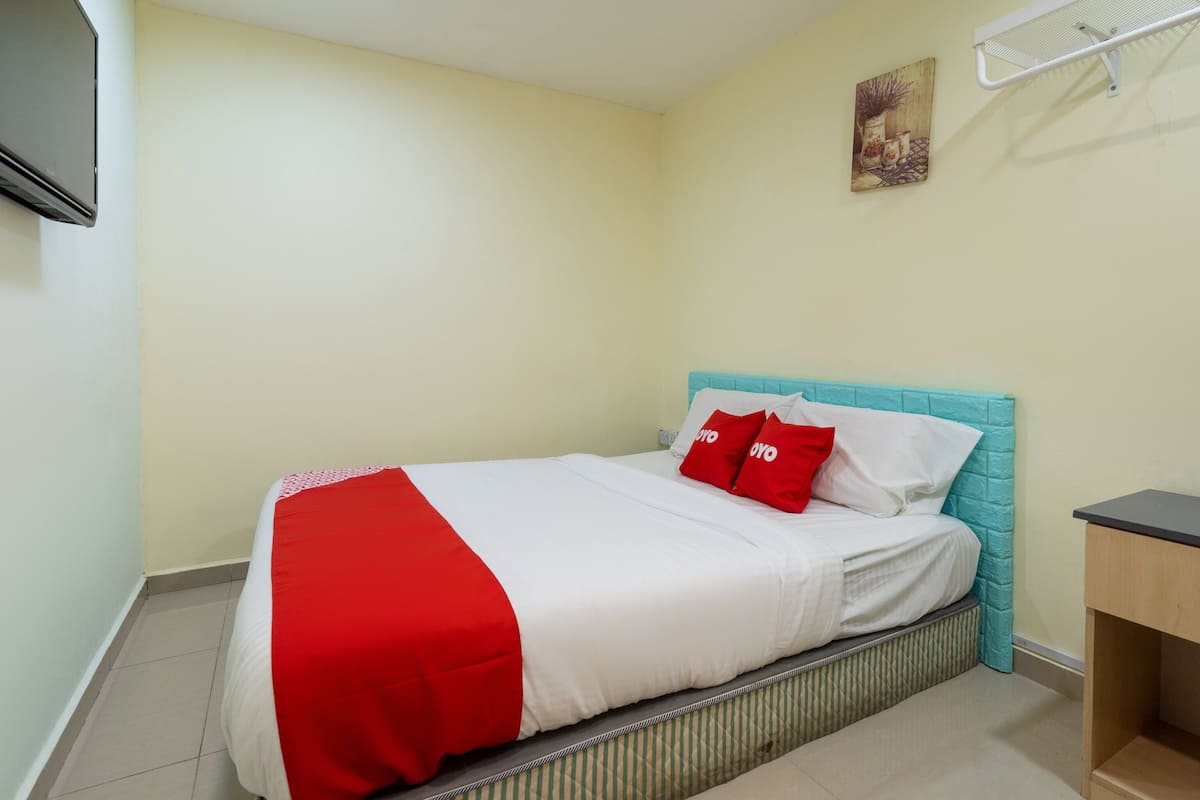 A neatly made bed with red and white bedding, a teal headboard, and a small bedside table.