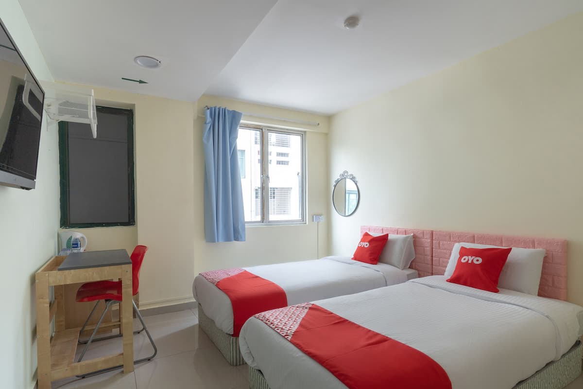 A hotel room with two beds, a desk, a chair, a TV mounted on the wall, and a window with curtains.