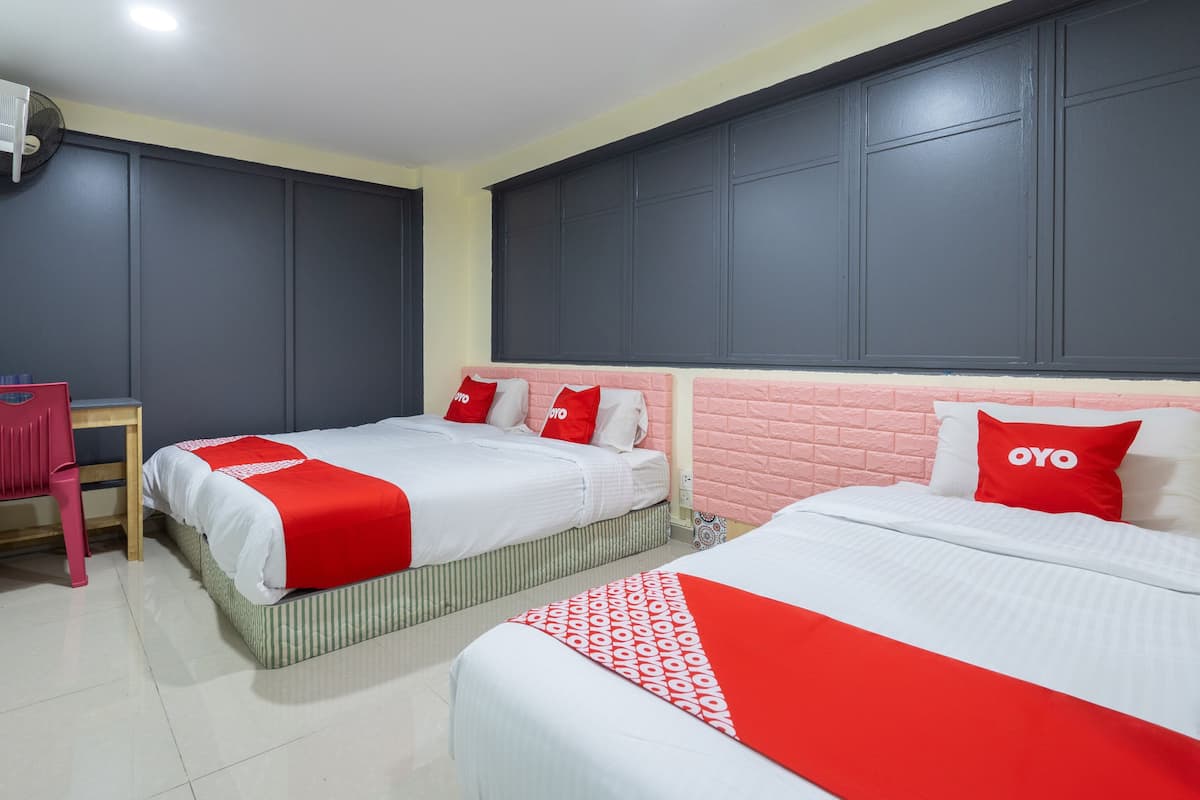 A hotel room with two beds, each with red and white bedding and pillows, a desk with a chair, and a ceiling fan.