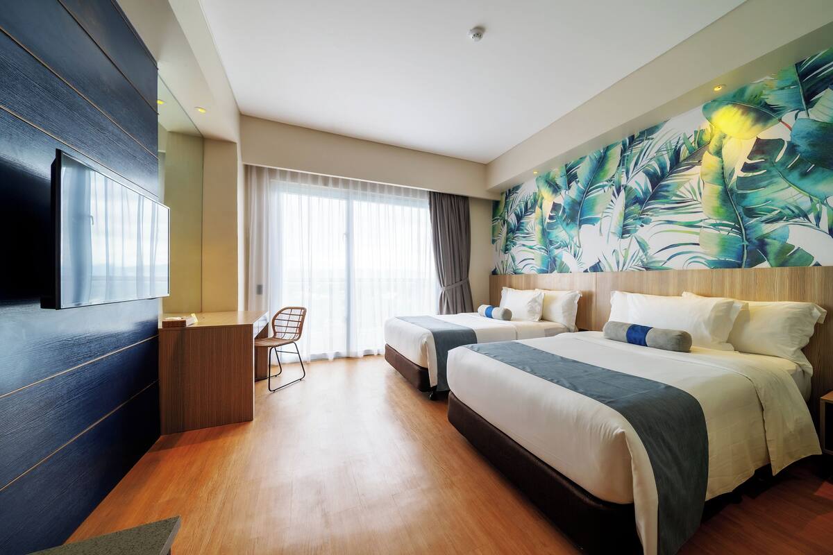 A hotel room with two beds, a desk, a chair, and a large window with curtains.