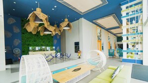 A modern lobby with a green sofa, wicker chairs, a wooden table, and a blue ceiling with leaf patterns. - Solea Palm Resort Mactan (Cordova)