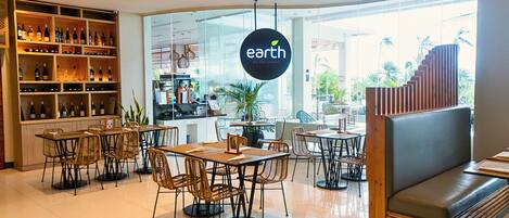 A restaurant interior with a large glass wall, wooden shelves with bottles, and a sign that reads 'earth ALL DAY DINING'.