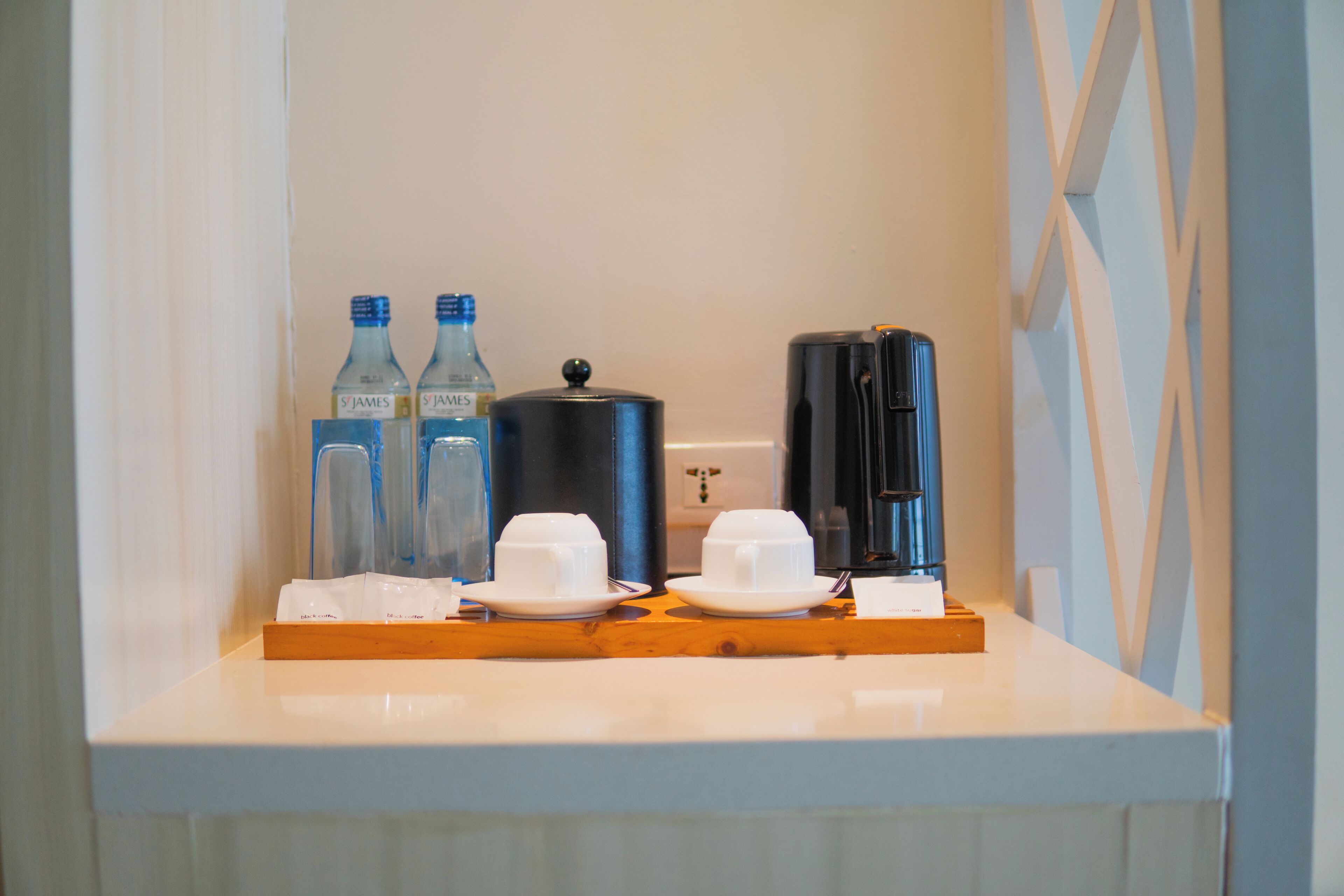 A breakfast bar with water bottles, a coffee maker, and white cups and saucers.
