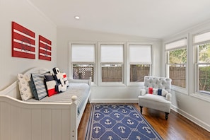 Relax in a nautical-themed room with a comfortable bed, anchor-patterned rug, and a plush armchair by the window.