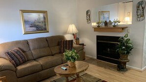 A living room with a brown sofa, a round wooden coffee table, a fireplace, and a painting on the wall. - Laurel Inn 411 is a beautiful condo with private balcony close to downtown (Gatlinburg)