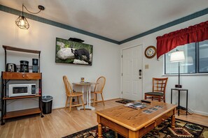 A cozy living room with a wooden coffee table, two chairs, a television mounted on the wall, a clock, and a red curtain. - Laurel Inn 411 is a beautiful condo with private balcony close to downtown (Gatlinburg)